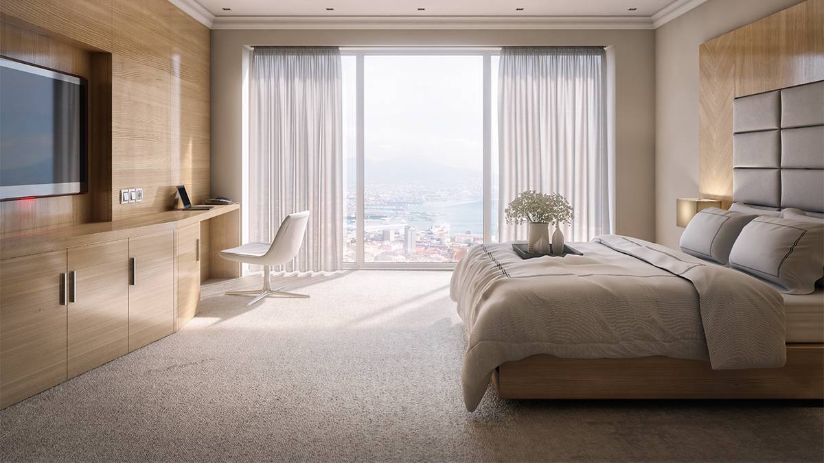 View of a very clean beige and brown hotel room with flowers on the bed and a large window with the curtains open on.